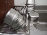 Des casseroles et poêles en argent sont empilées dans un évier équipé d'un égouttoir.