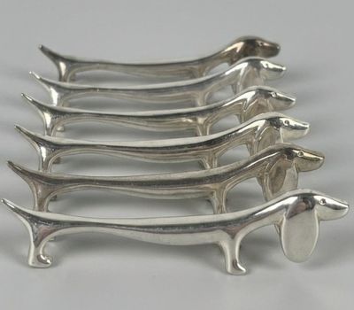 six teckels en métal plaqué argent sont alignés sur une surface blanche