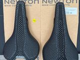 deux selles noires percées de trous, dans une boîte en carton