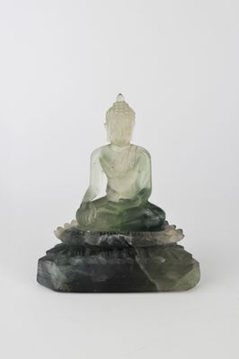 une statue de Bouddha en jade vert, assise sur un rocher, sur fond blanc