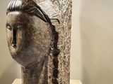 sculpture of a woman ' s head on a pedestal in front of a wall