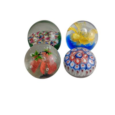 quatre presse-papiers en verre de couleurs et de motifs différents sur fond blanc