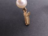 a white pearl and a gold pin on a black surface