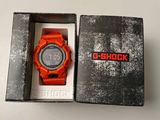 une montre orange dans un coffret posé sur une surface blanche