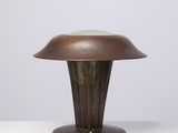 une lampe de table en bronze posée sur une surface blanche, sur fond gris