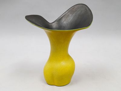 un vase jaune contenant une cuillère, posé sur une surface blanche