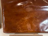 brown leather purse sitting on top of a toilet seat next to a roll of toilet paper
