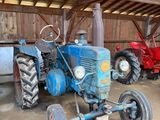 un tracteur bleu garé dans une grange avec d'autres tracteurs
