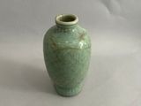 un petit vase vert posé sur une surface blanche