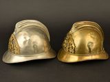 pair of gold and silver fire helmets on a black background