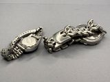 two pieces of silver jewelry on a gray surface