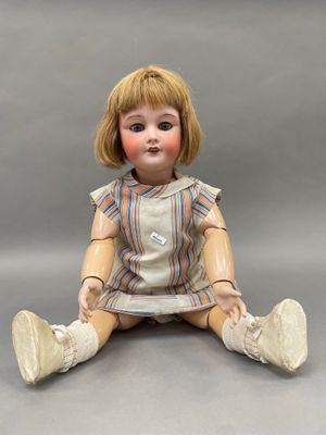 une petite poupée assise par terre, les jambes croisées