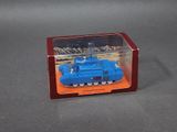 un petit char de jouet bleu dans une boîte transparente posée sur une surface grise