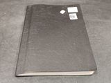 an open black book with a tag on it sitting on a table