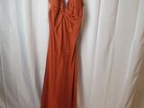 une robe orange suspendue à un cintre devant un fond blanc