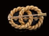 an image of a gold colored brooch with a knot around it