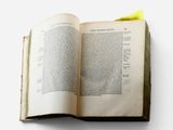 an open book on a white surface with a yellow post sticking out of it