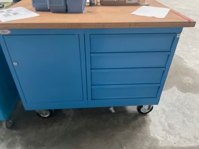 une armoire bleue avec un plateau en bois, montée sur roulettes, dans un entrepôt