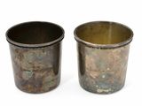 deux vieilles tasses en métal posées l'une à côté de l'autre sur une surface blanche