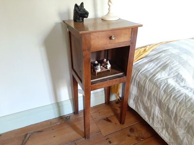 une petite table en bois sur laquelle est posée une lampe, à côté d'un lit