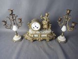 une horloge posée sur une table, à côté de trois chandeliers
