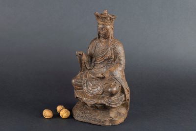 une statue représentant une femme assise sur un rocher, avec des noix devant elle