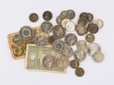 un tas de pièces et un billet de banque posés sur une surface blanche