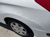 a white car with a red tail light on the side of the road
