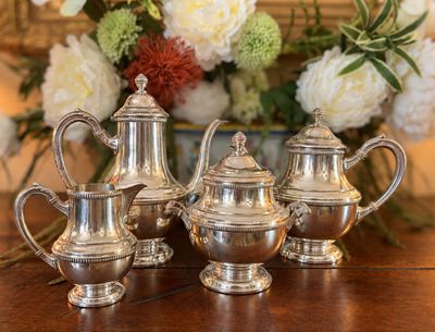trois théières en argent posées sur une table, à côté d'un vase de fleurs