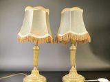 pair of gold table lamps with fringed lampshads on a black table