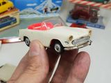 a hand holding a toy car in front of a box of toys
