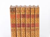 six old books are stacked on top of each other on a white surface