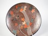 une assiette marron ornée de feuilles orange et vertes, posée sur un support