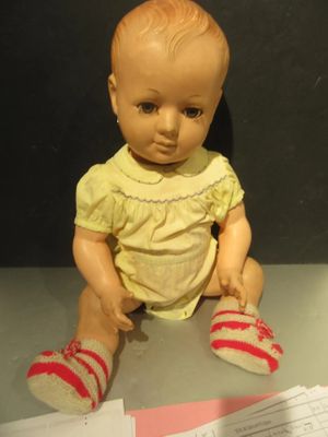 a baby doll sitting on a table with a sheet of paper
