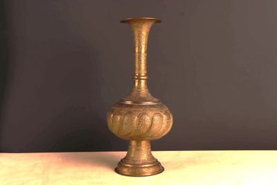 un vase doré posé sur une table, avec un mur noir en arrière-plan