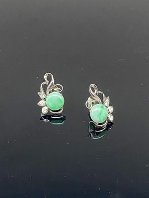 une paire de boucles d'oreilles en jade vert et diamants posées sur un fond noir