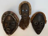 three african masks hanging on a wall with a person standing in front of them