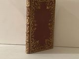un petit livre rouge aux bords dorés posé sur une table blanche