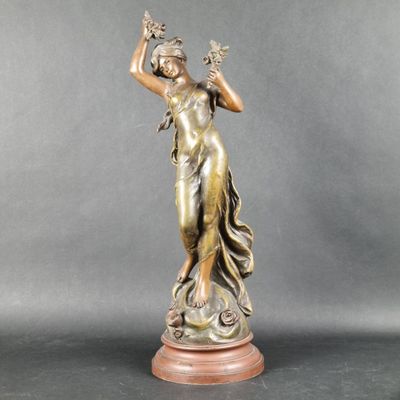 une statue antique en bronze représentant une femme tenant une fleur à la main