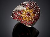 a close up of a ring with red and yellow stones on a black surface