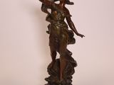 statue en bronze représentant une femme tenant un oiseau, posée sur un socle en bois