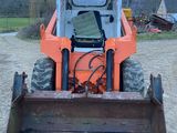 une photo d'un petit tracteur orange garé sur un terrain en terre battue