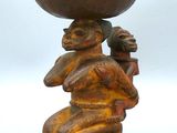 une sculpture en bois représentant une femme tenant un bol en équilibre sur la tête