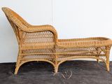 a wicker chaise lounger on the floor next to a white wall