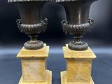 paire d'urnes anciennes en bronze reposant sur des socles en marbre, sur fond noir