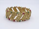 a close up of a gold bracelet with green and red stones