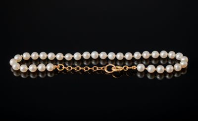 un collier de perles à un rang avec un fermoir en or sur fond noir