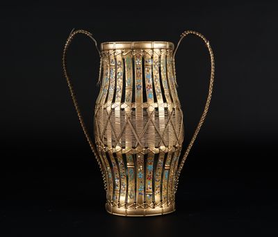 un vase doré posé sur une surface noire, avec un fond noir
