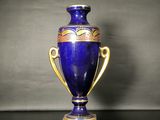 un vase bleu posé sur une table, muni d'une anse dorée
