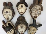 cinq masques africains sont disposés en cercle sur une surface blanche